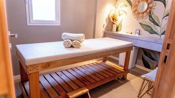 A wooden massage table with a white mattress, a wooden bench, and a small step stool.
