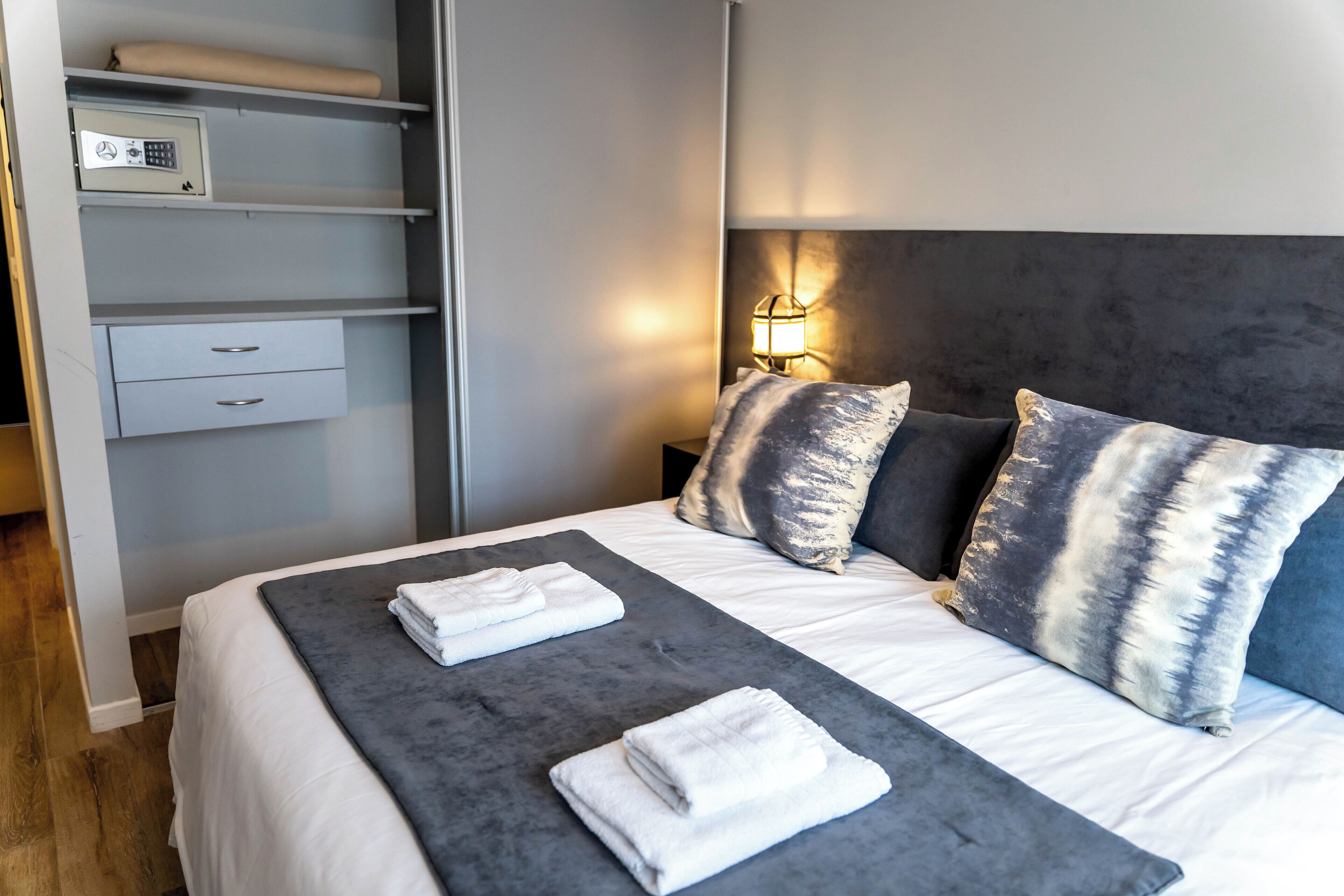 A hotel room with a bed, a nightstand, a lamp, a wardrobe, and a small safe.