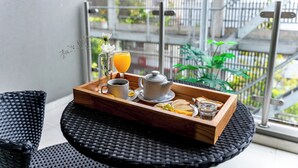 A breakfast tray with a teapot, cup, orange juice, and toast on a wicker table with a view of a balcony and railing. - O2 Hoteles Mar del Plata (Mar del Plata)