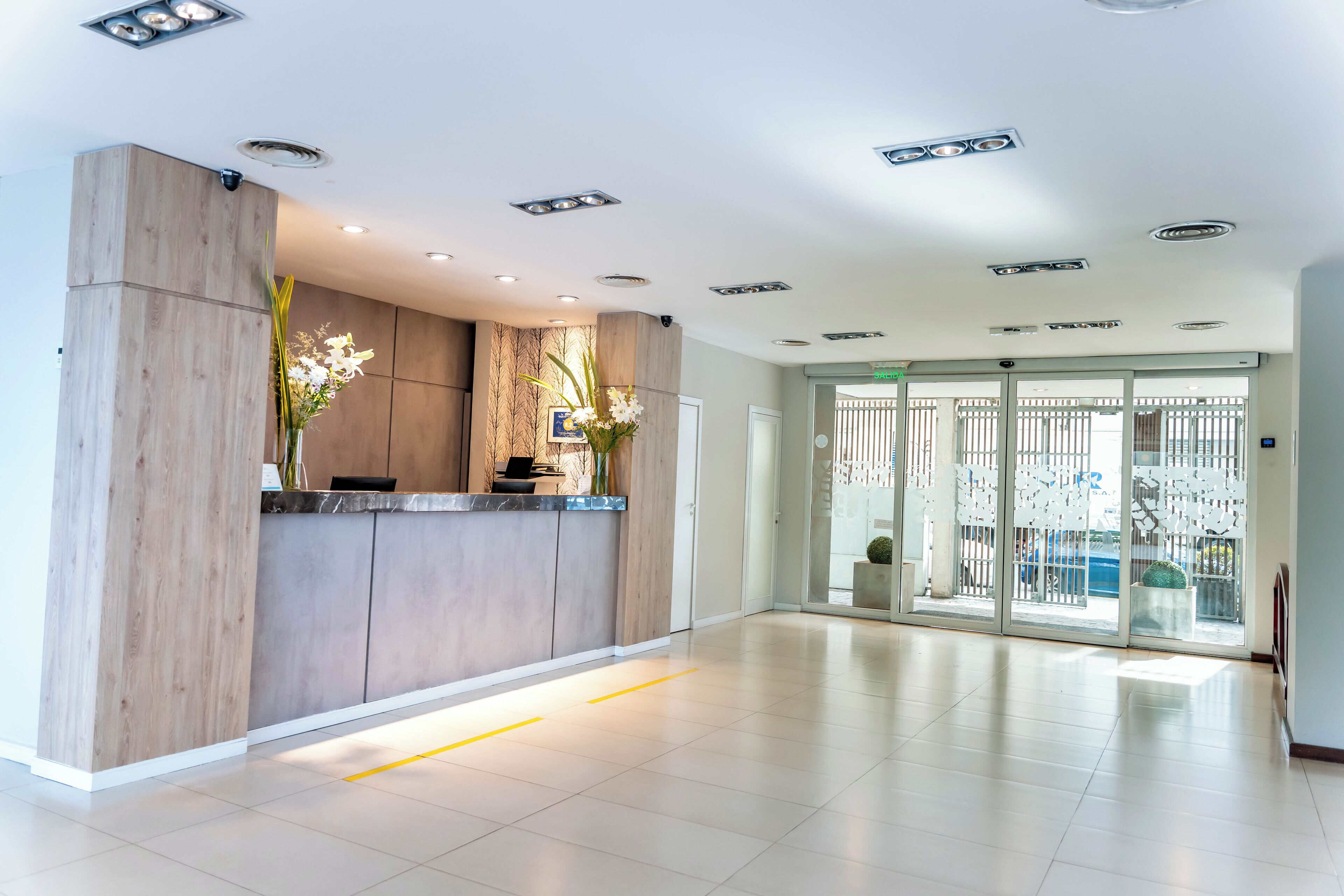 A modern reception area with a wooden reception desk, a glass door entrance, and a view of the outside.