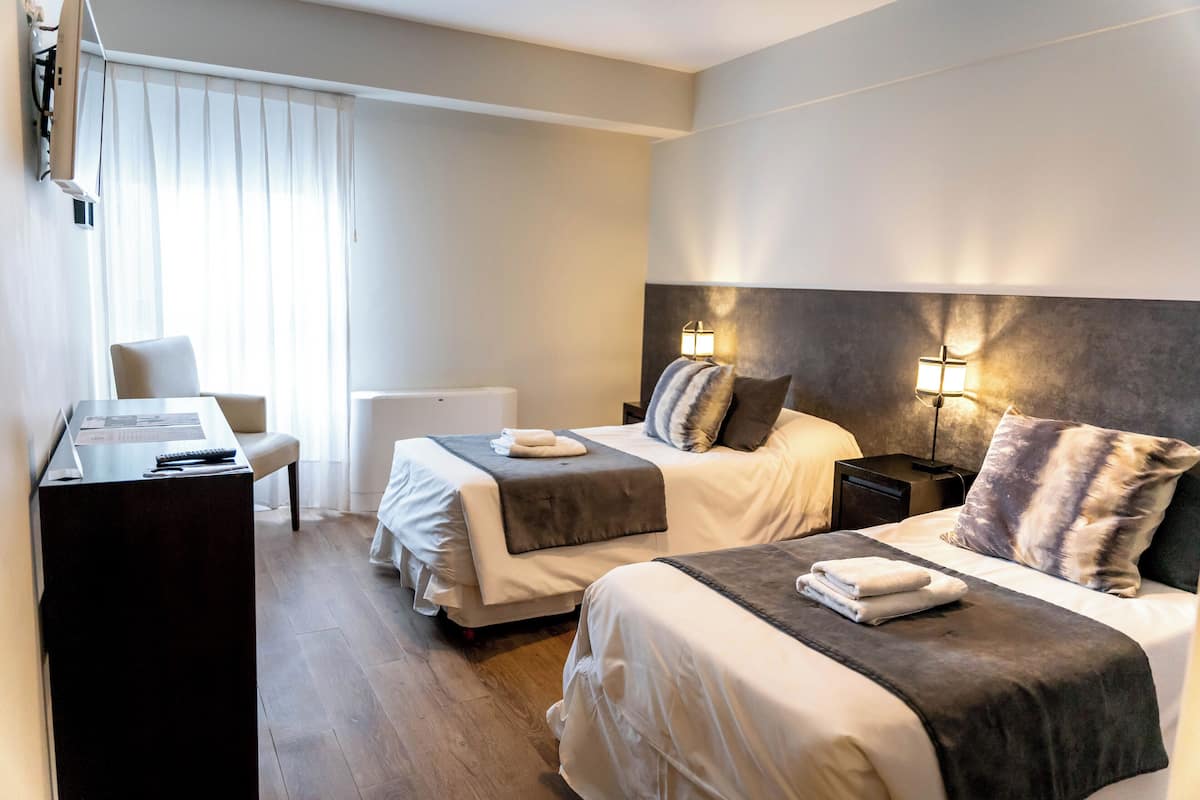 A hotel room with two beds, a desk, a chair, and a bedside table.