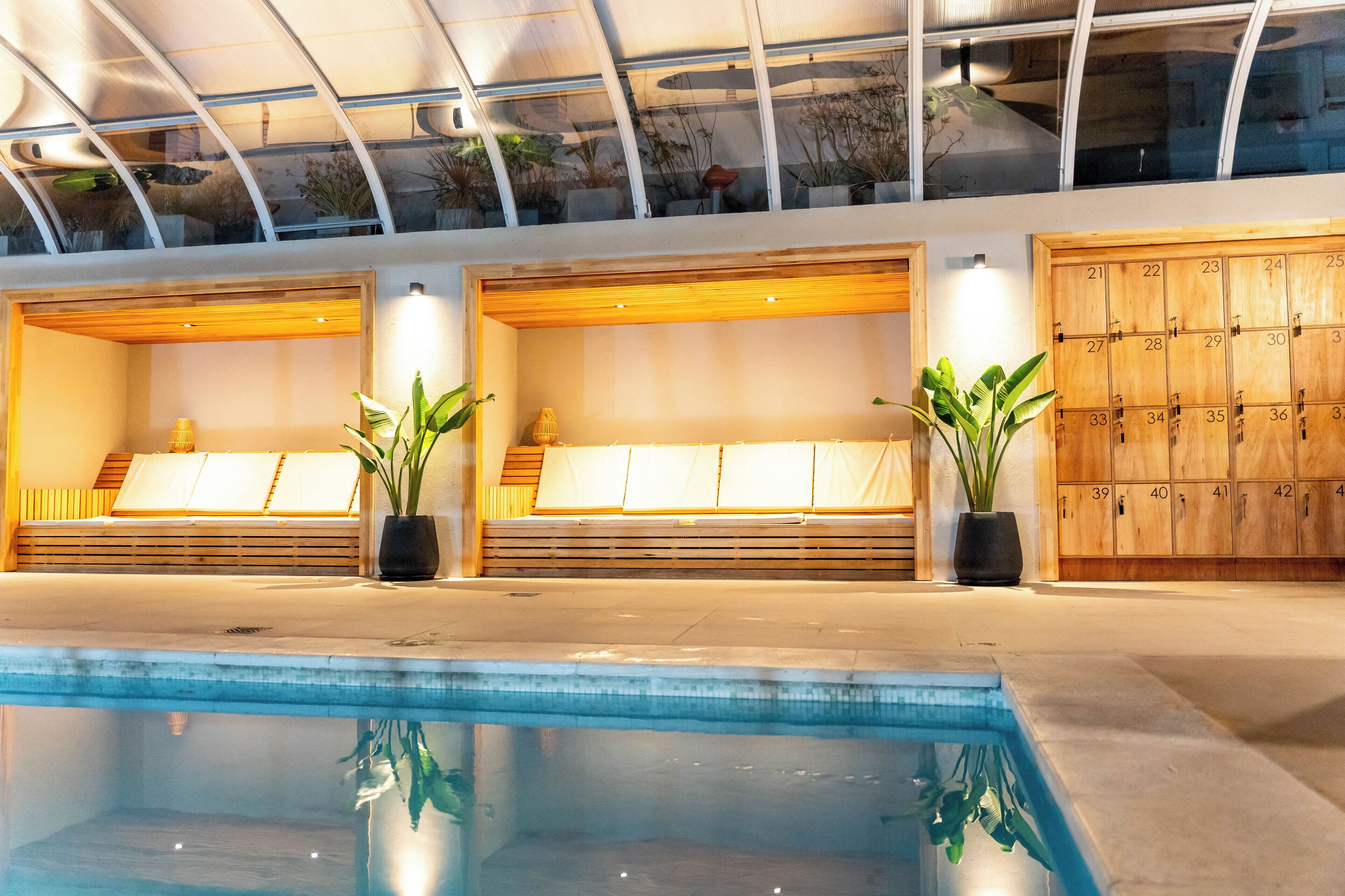 A modern indoor pool area with seating and lockers.
