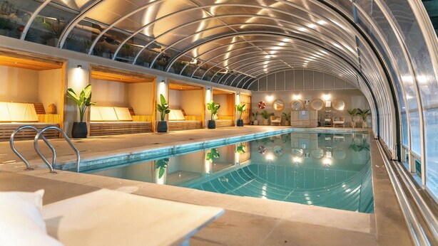 An indoor swimming pool with a glass ceiling, seating areas, and potted plants. - O2 Hoteles Mar del Plata (Mar del Plata)