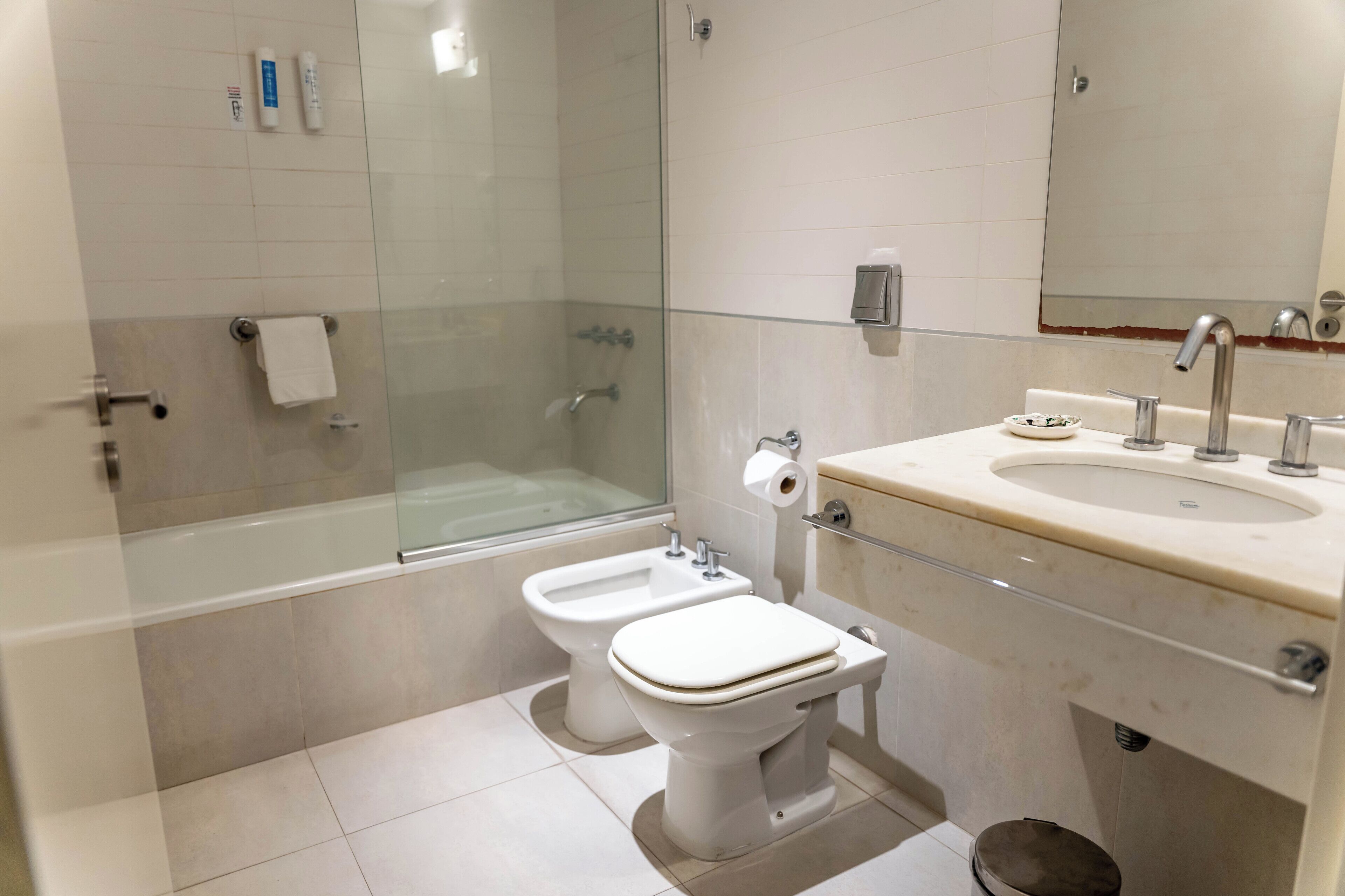 A modern bathroom with a glass-enclosed shower, a toilet, a bidet, and a sink with a mirror.