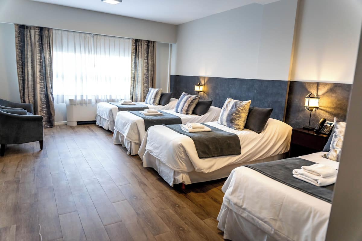 A hotel room with three beds, a sofa, and a large window with curtains.