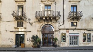 A historic building with ornate balconies, a central entrance, and a small shop on the ground floor. - Duomo Suites & Spa (Catania)