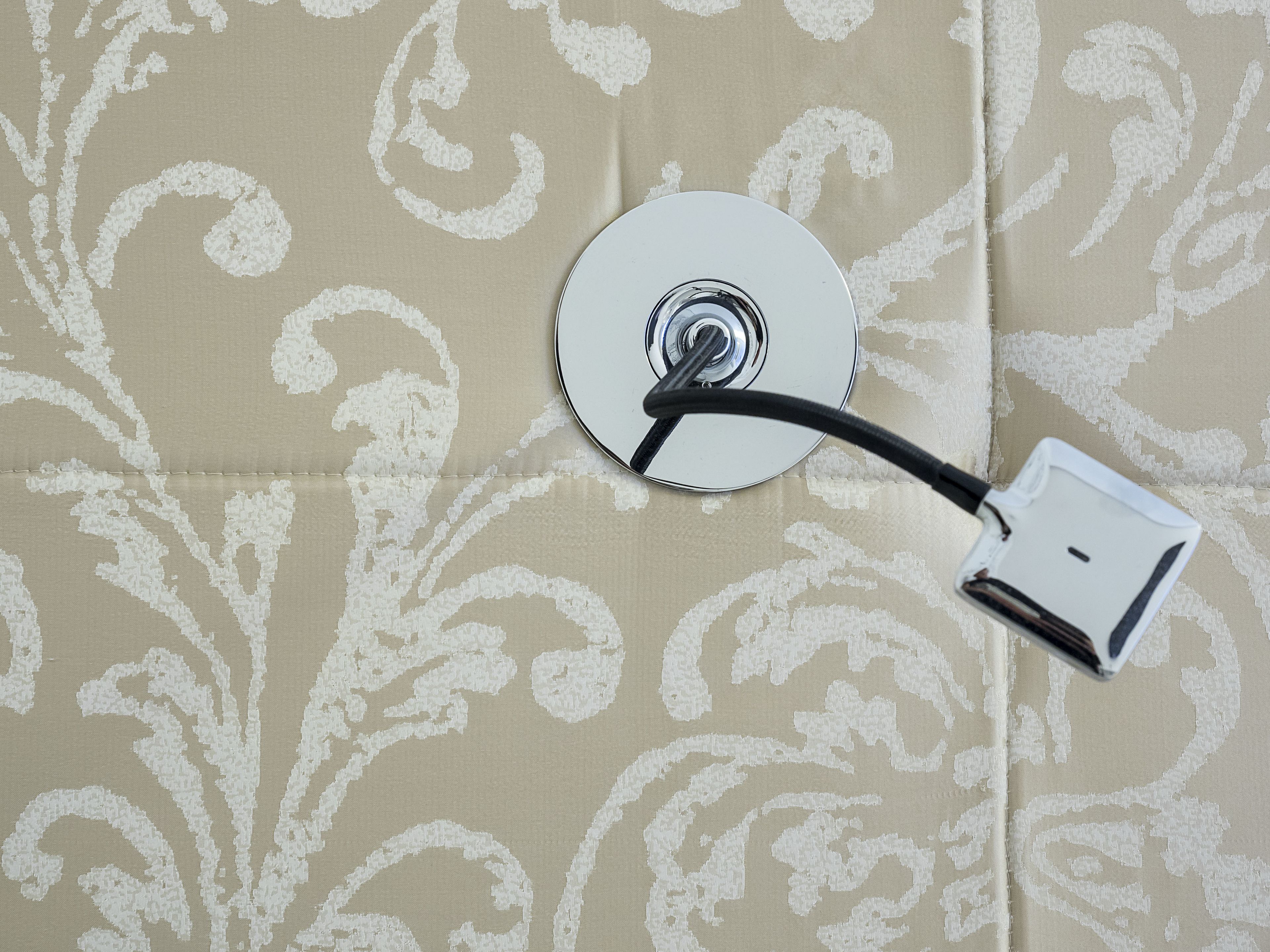 A close-up of a white circular object with a black cable attached, set against a beige patterned background.