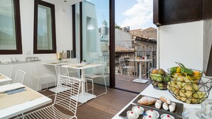 A modern dining area with white furniture, a balcony with a view of buildings, and a fruit basket on the table. - Duomo Suites & Spa (Catania)