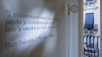Una pared con una cita en italiano, una ventana que ofrece vista a un edificio y una puerta con pomo circular.