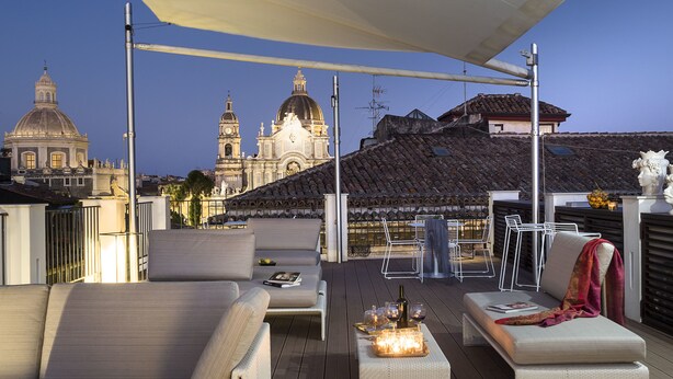 A rooftop terrace with seating, a table with candles, and a view of historic buildings. - Duomo Suites & Spa (Catania)