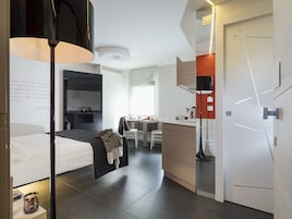 Camera d'albergo moderna con un letto, comodino, lampada e vista sull'area cucina.