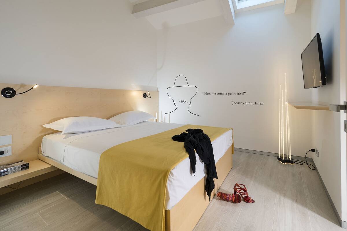 A modern bedroom with a bed, a wall art piece, a TV, and a window.