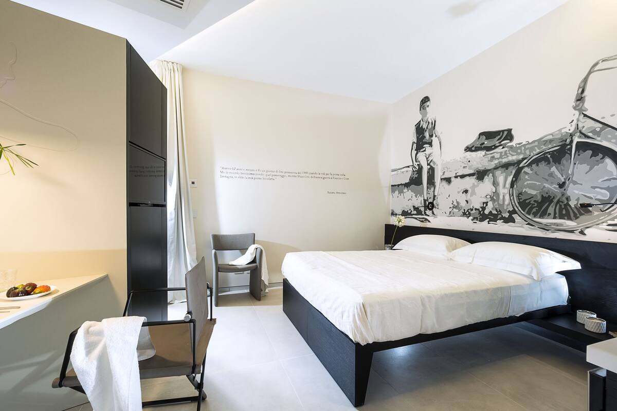 A modern hotel room with a bed, a chair, a desk, and a large wall mural.