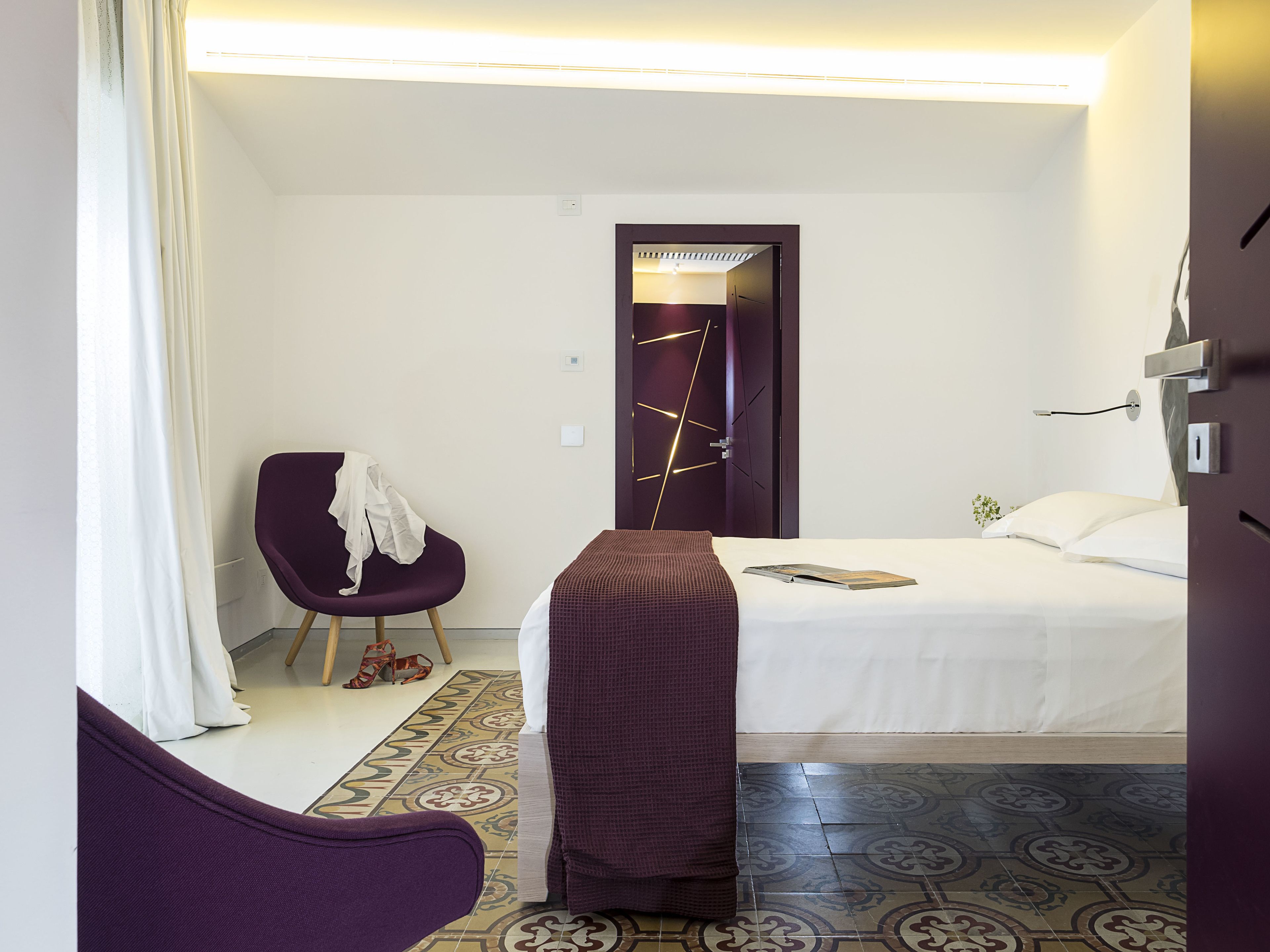 Habitación de hotel con cama, una silla, mesita de noche y puerta con lámpara moderna.