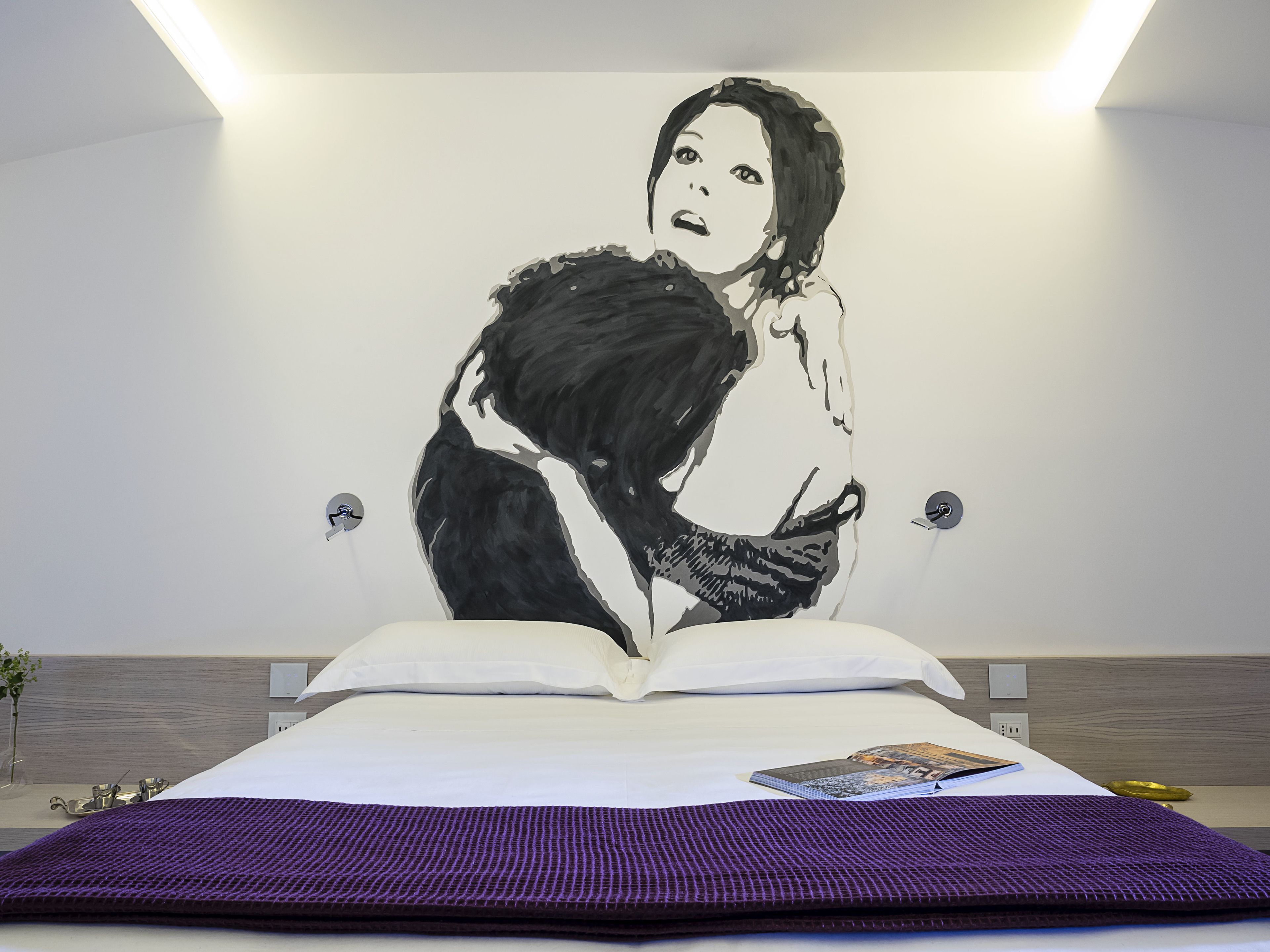 A bedroom with a large bed, a purple throw blanket, and a book on the bed.