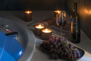 Un'ambientazione rilassante da spa con vasca idromassaggio, candele, una bottiglia di vino e grappoli d'uva.