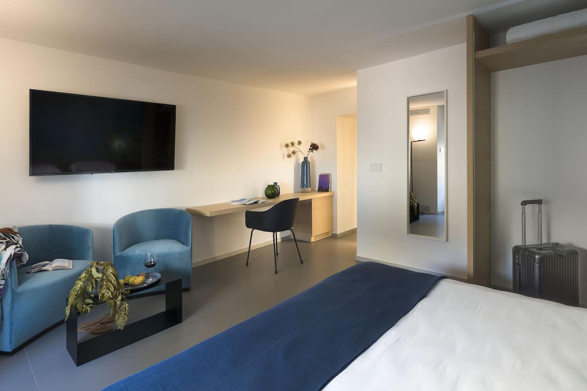 A modern hotel room with a bed, a desk, a chair, a TV, and a suitcase.