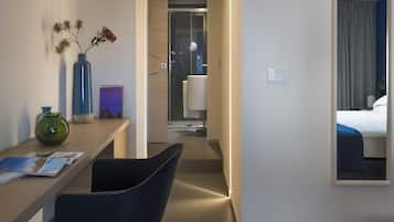 Una camera d'albergo con una scrivania in legno, una sedia, un vaso con fiori secchi, un quadro incorniciato e un letto con copriletto blu.