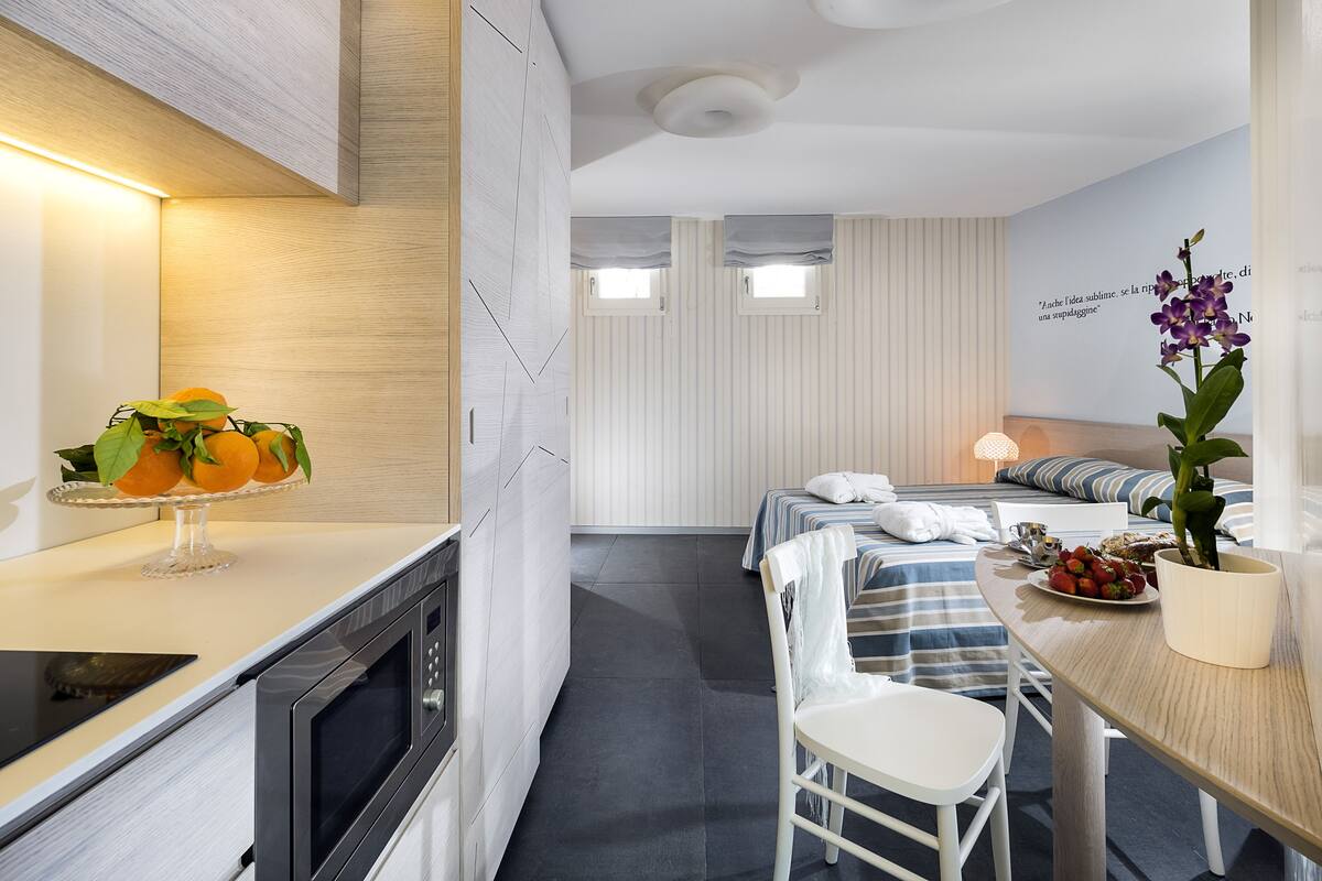 A modern hotel room with a kitchenette, a dining area, and a bed with a view.