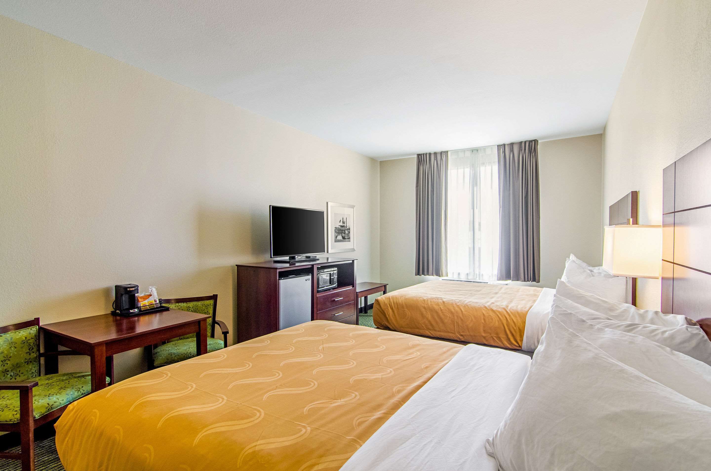 Habitación de hotel con dos camas, un escritorio, televisión, cafetera y ventana con cortinas.