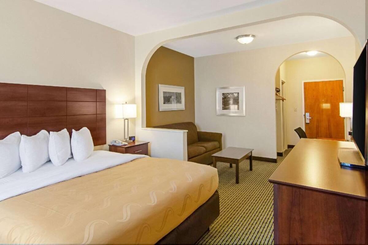 A hotel room with a large bed, a desk, a chair, and a sofa.