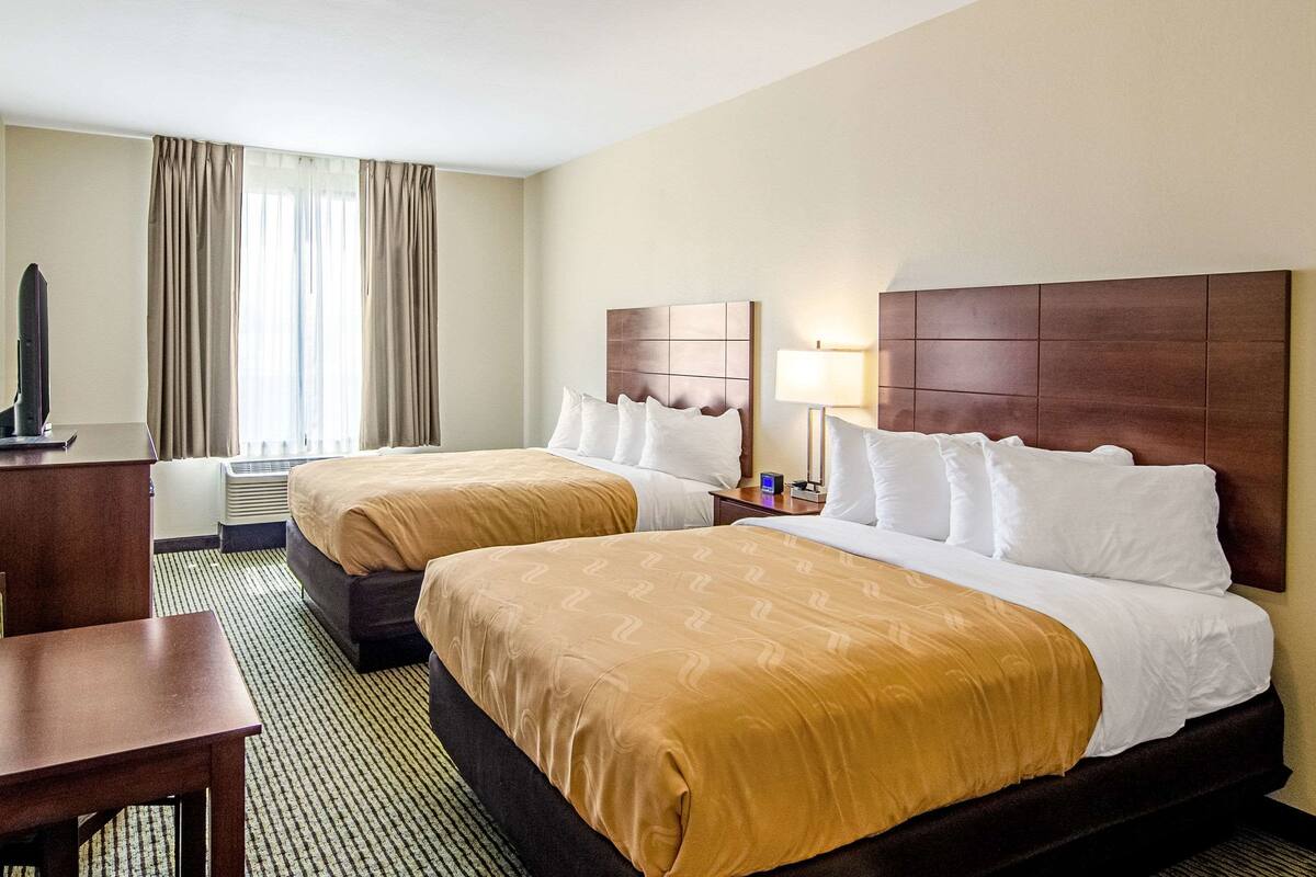 A hotel room with two beds, a desk, a TV, and a window with curtains.
