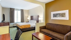 A hotel room with a bed, a sofa, a desk, a television, and a framed picture on the wall. - Quality Inn & Suites Near Tanger Outlet Mall (Gonzales)