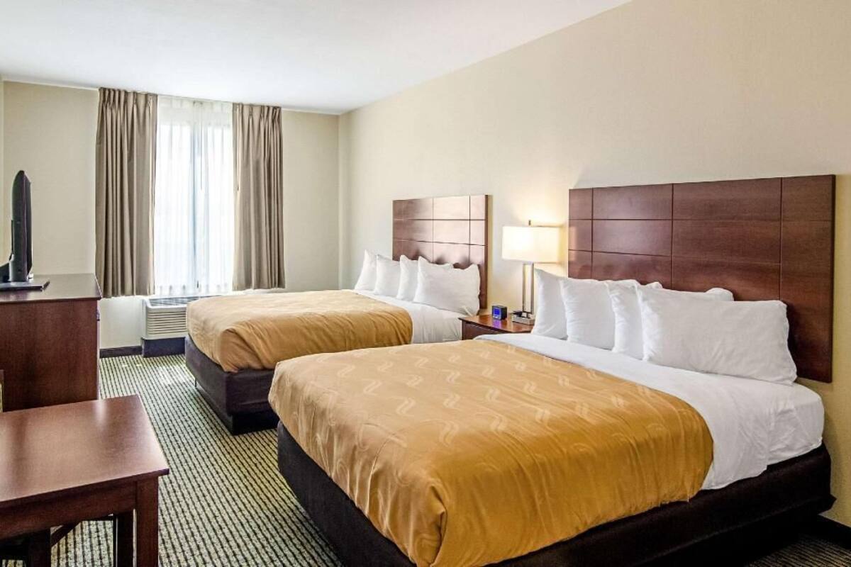 A hotel room with two beds, a desk, a TV, and a window with curtains.