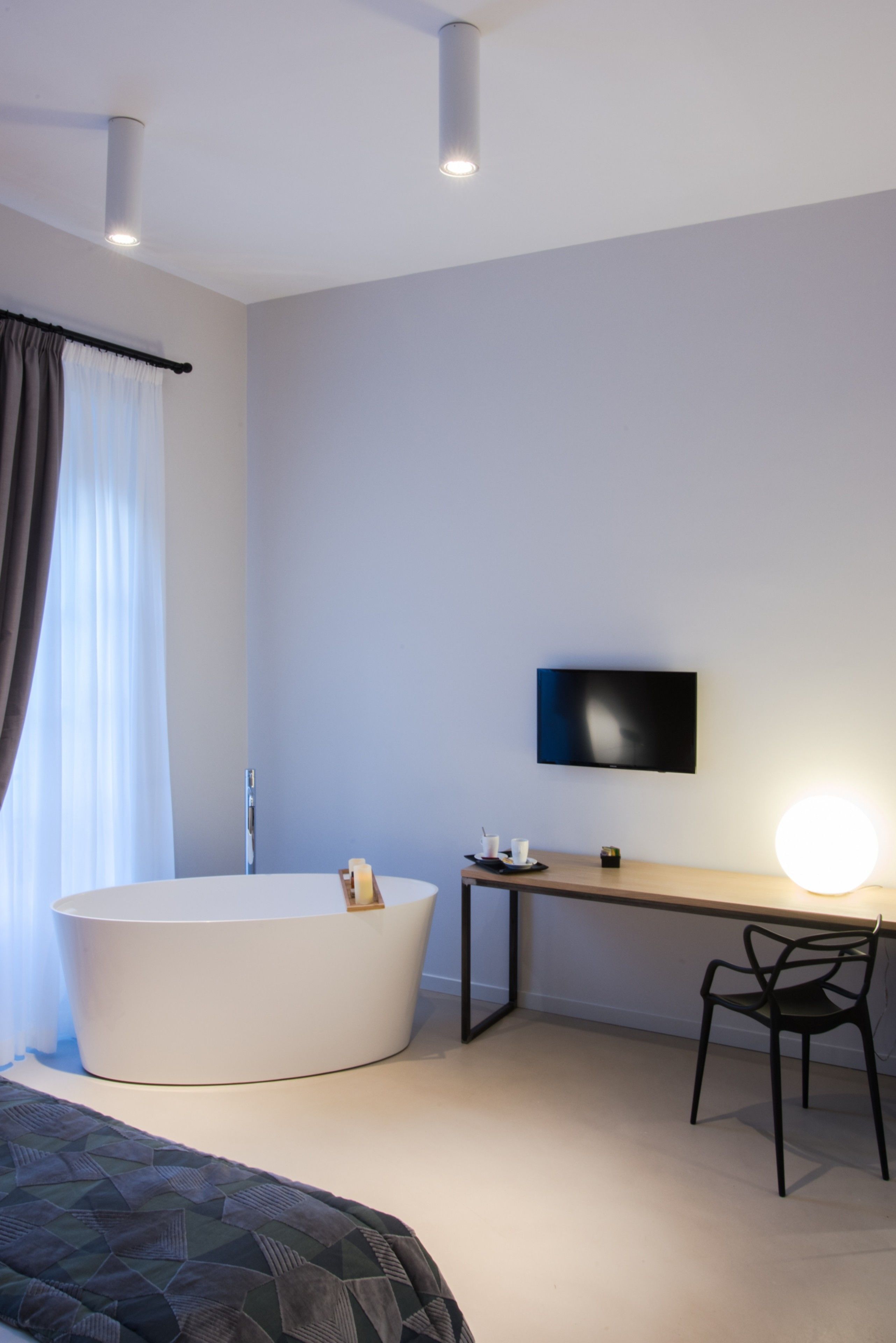 A modern bedroom with a large white bathtub, a desk with a flat-screen TV, and a chair.