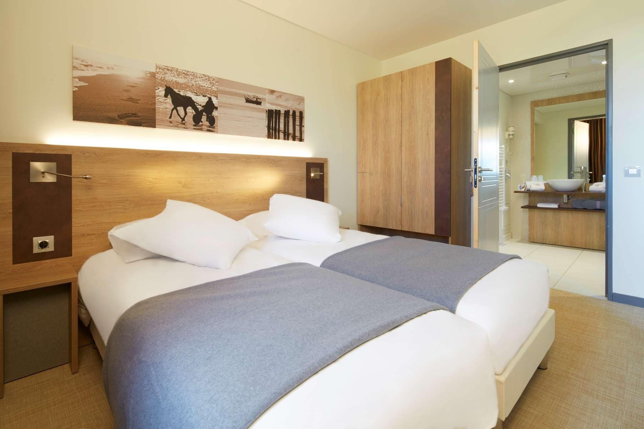 A hotel room with a bed, bedside tables, a mirror, and a bathroom visible through an open door.