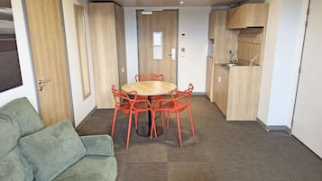 A compact living space with a round wooden table and orange chairs, a green sofa, and a kitchenette with wooden cabinets.