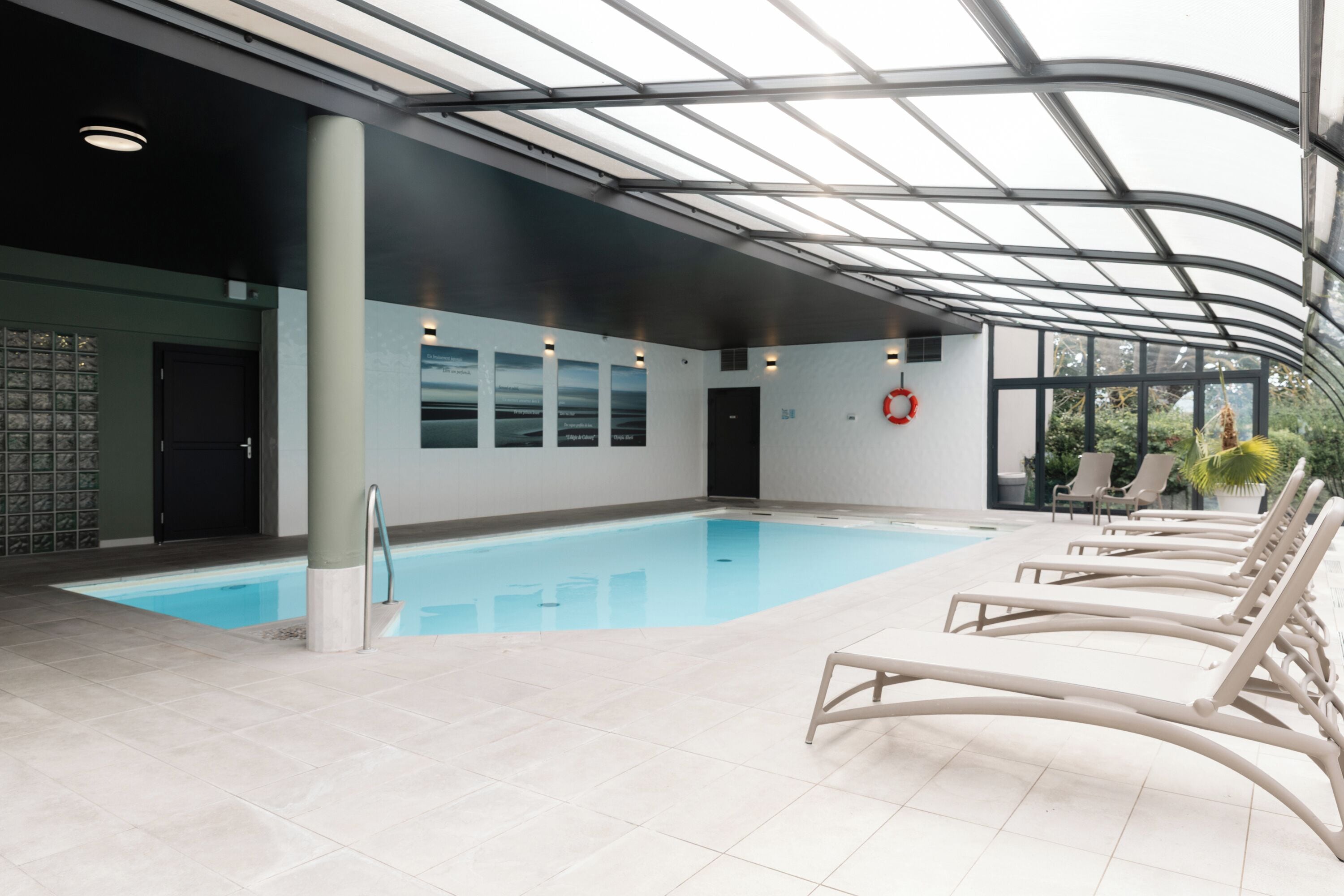 An indoor swimming pool with clear glass ceiling, lounge chairs, and a lifebuoy.