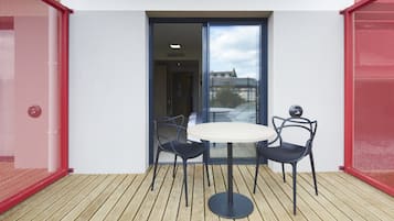 A small outdoor patio with a round table and two chairs, a sliding glass door, and a red mesh fence.