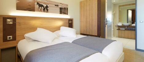 A modern hotel room with a large bed, a wooden headboard, a bedside table, and a bathroom visible through an open door.