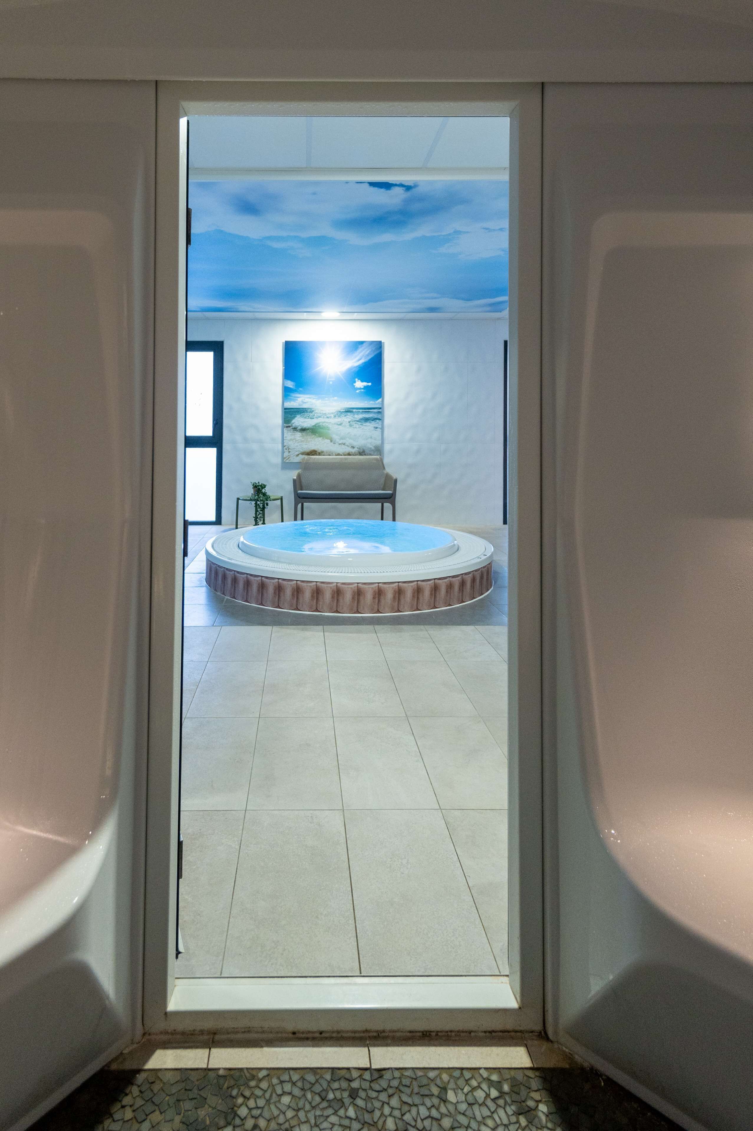 Un espace de détente avec un jacuzzi, une peinture représentant un ciel et un fauteuil.