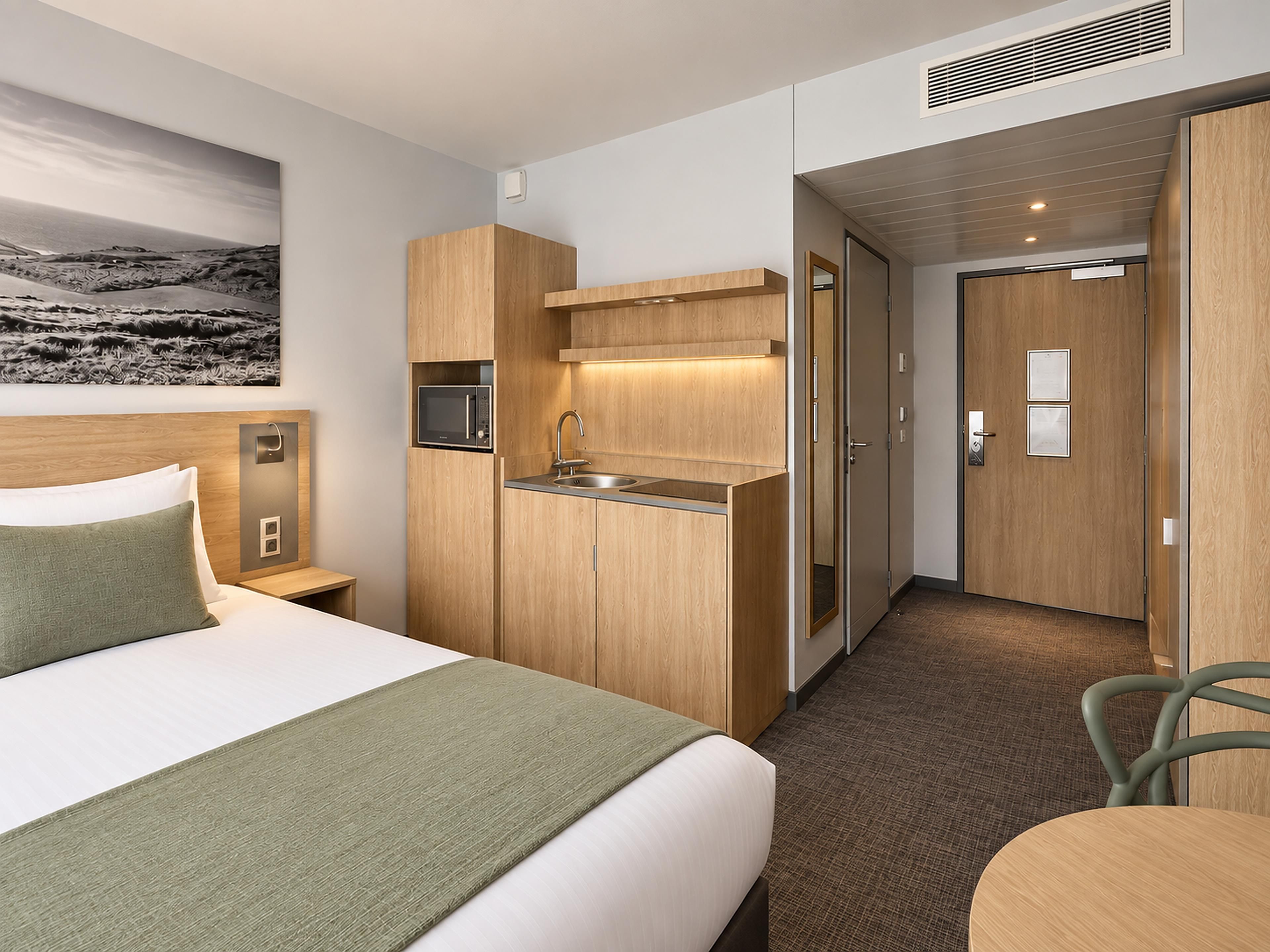 Ein Hotelzimmer mit Bett, einer kleinen Küchenzeile, einem Badezimmer und Meerblick.
