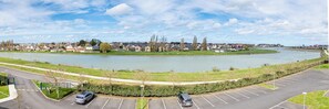 Un estacionamiento junto a un río, con vista a una zona residencial al fondo.