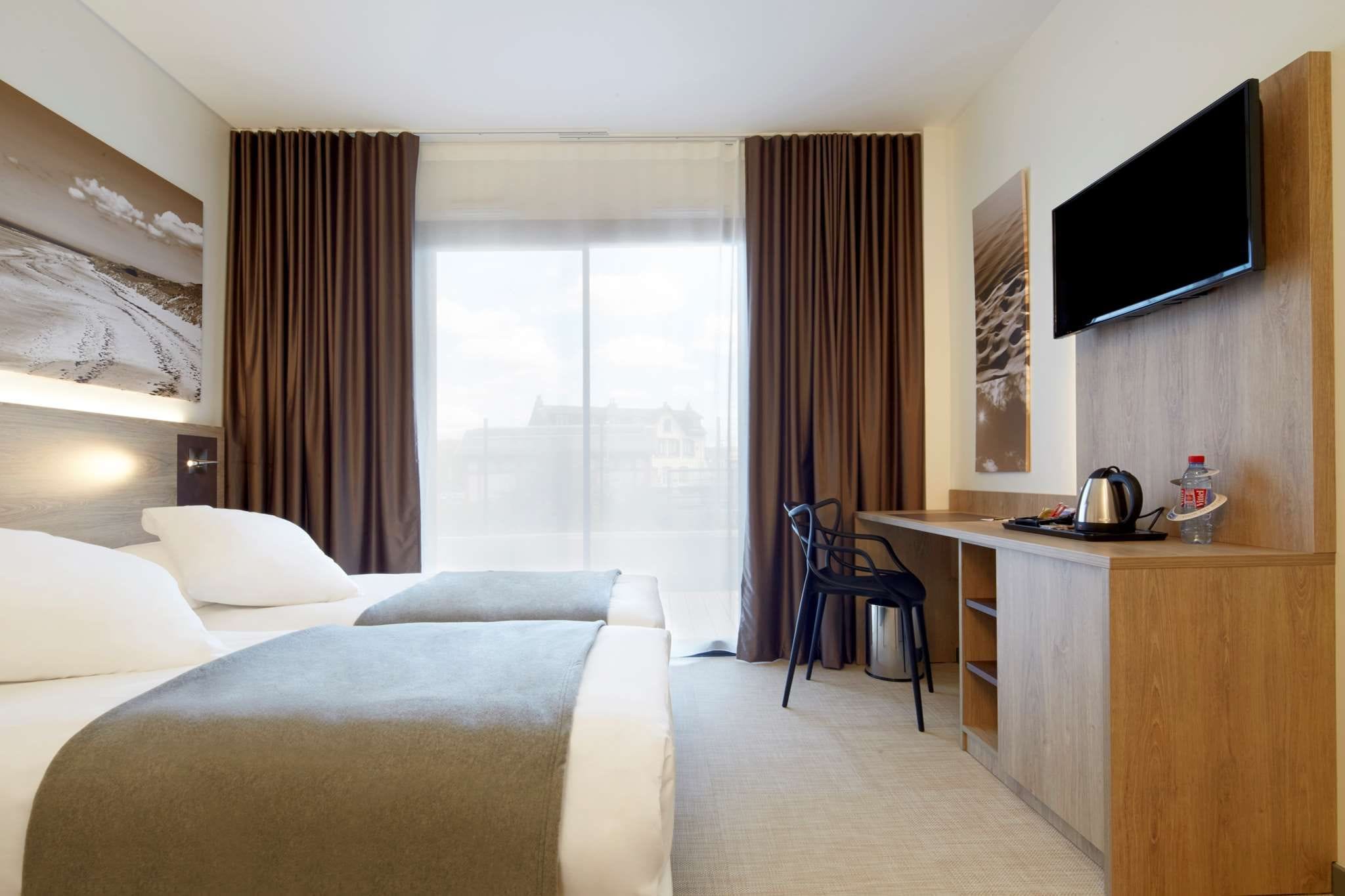 A hotel room with a bed, a desk, a chair, a television, and a window with curtains.