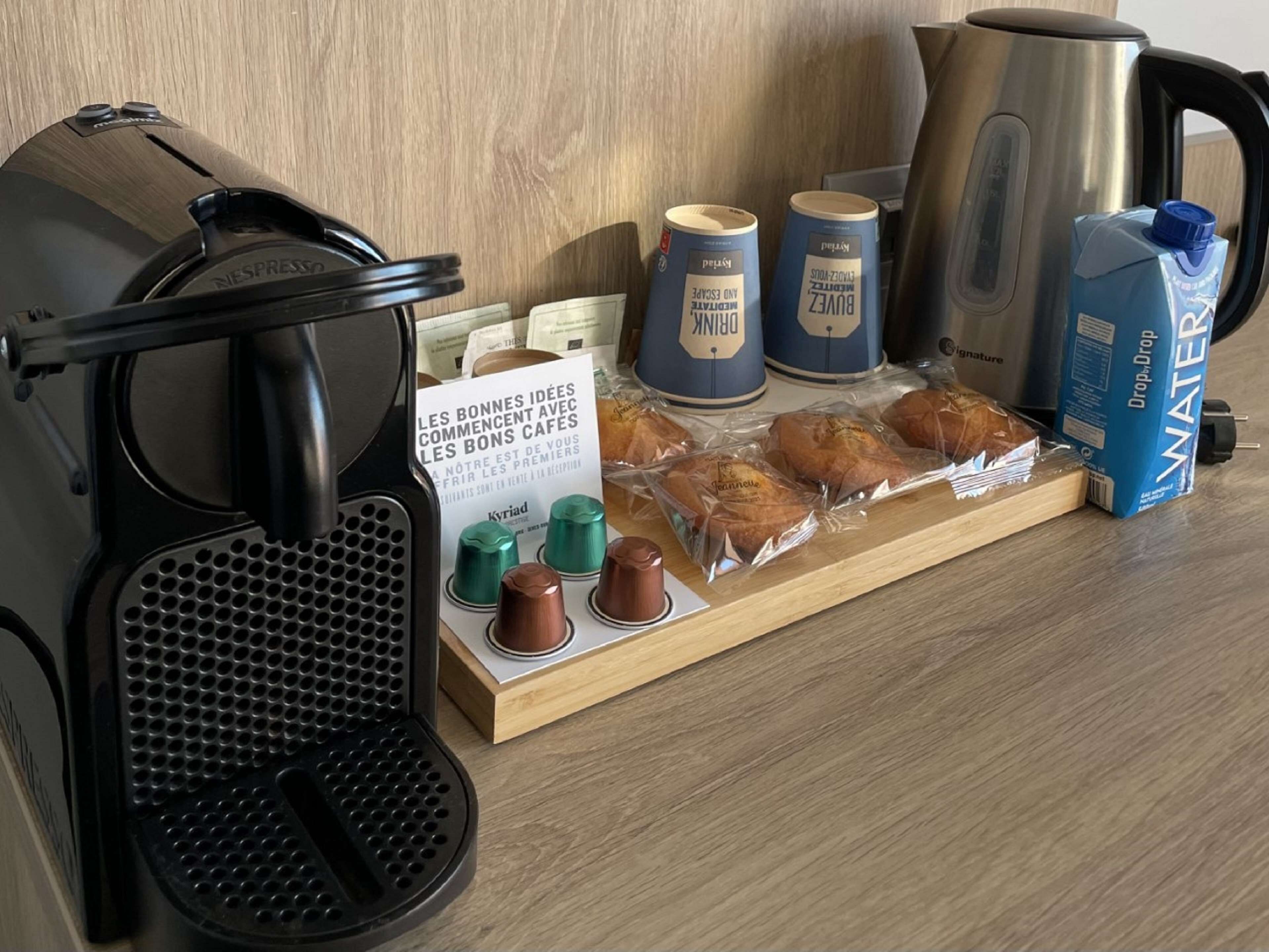 Máquina de café, jarra de água, cafeteira e pão embalado sobre uma superfície de madeira.