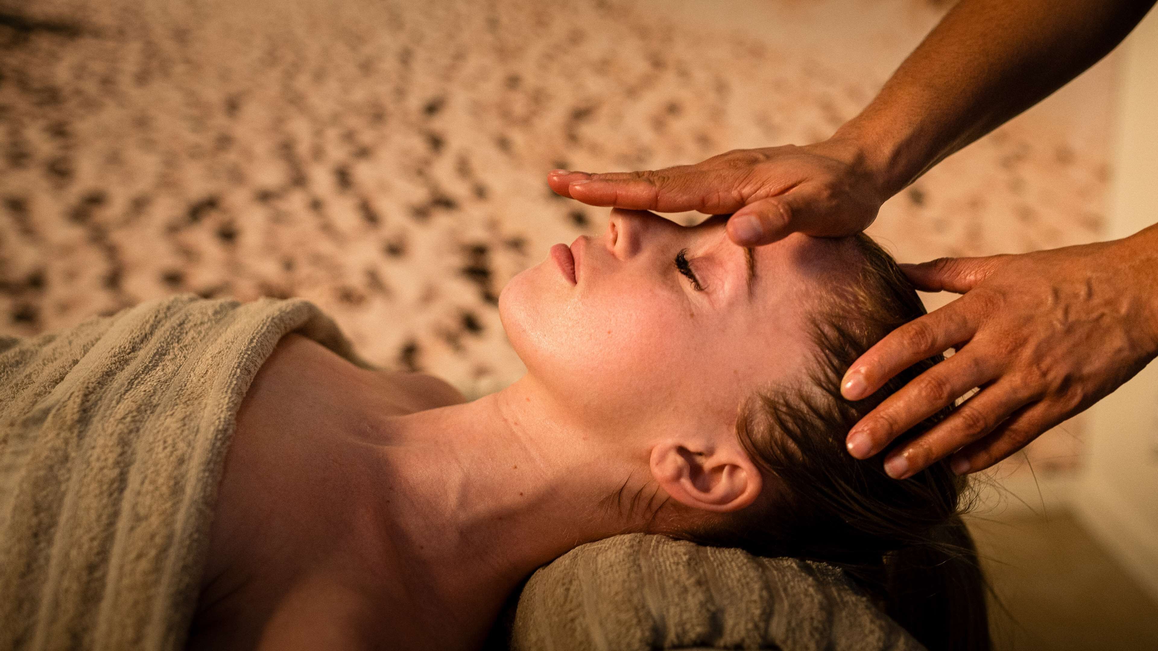 A person receiving a head massage on a sandy surface.