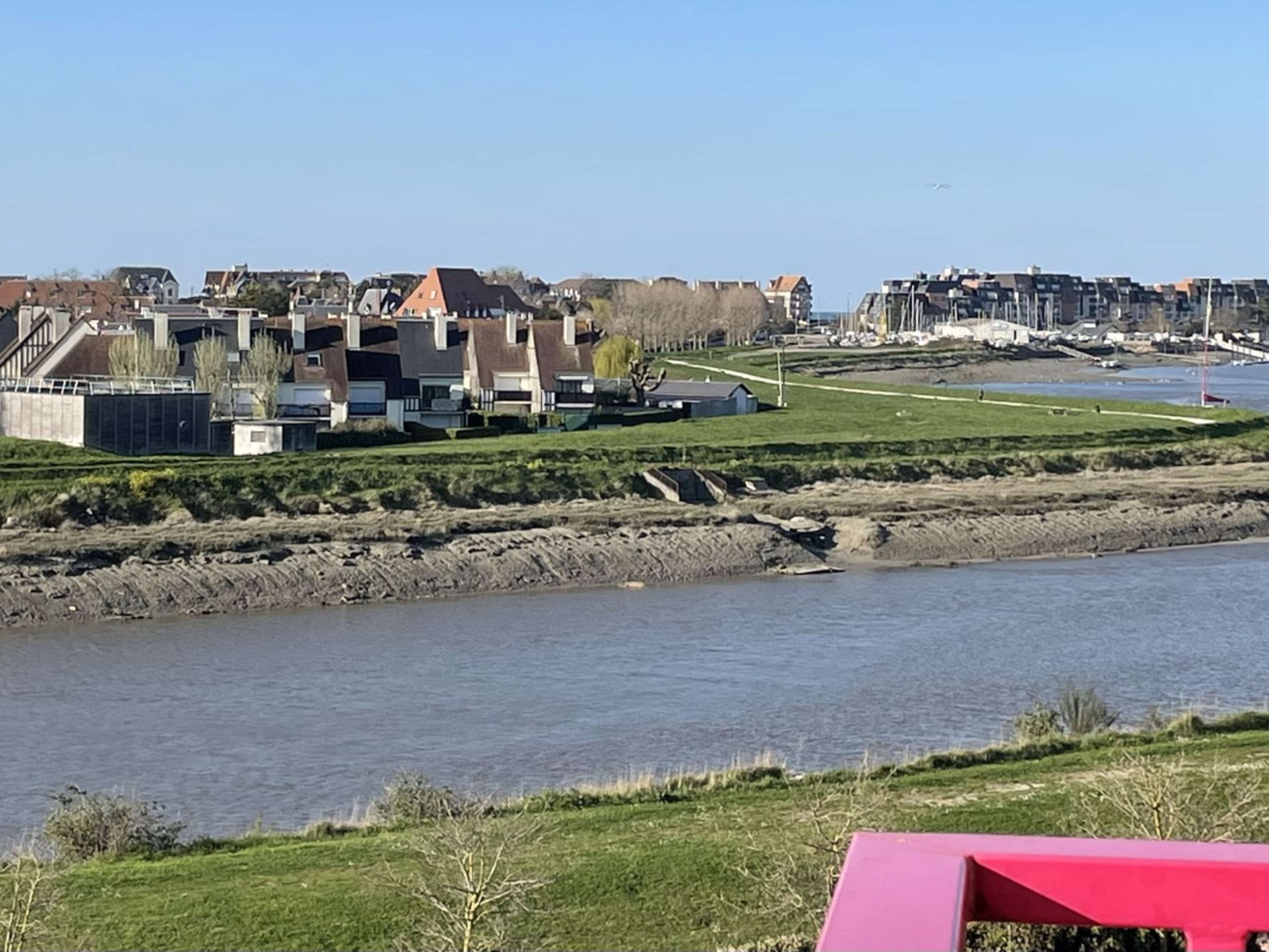 A riverside view with buildings, a red structure, and a clear sky.