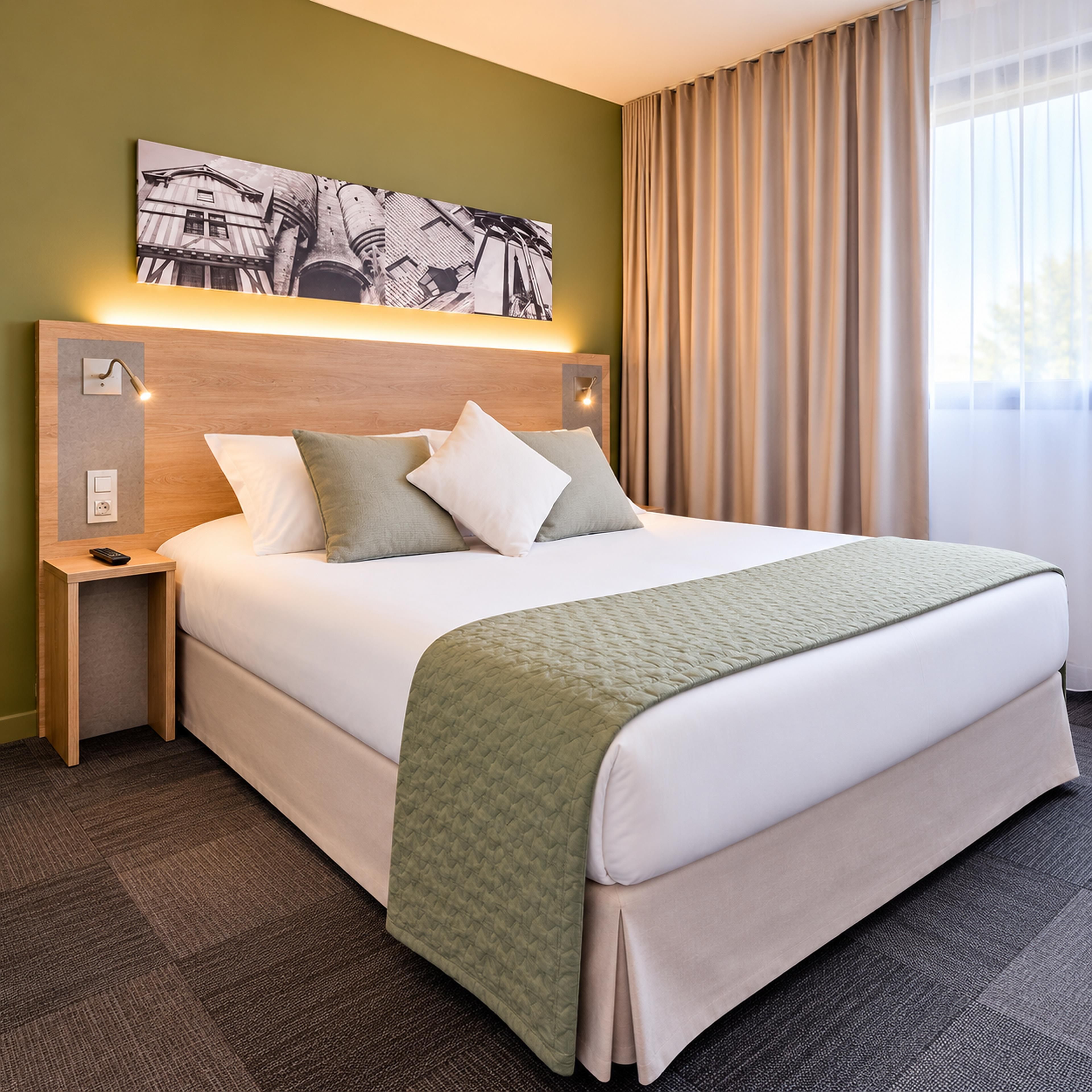 Habitación de hotel con una cama grande, cabecera con luces empotradas, mesita de noche y un cuadro sobre la cama.