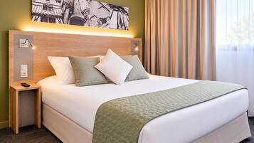 A hotel room with a large bed, a headboard with wall-mounted lights, a nightstand, and a painting above the bed.