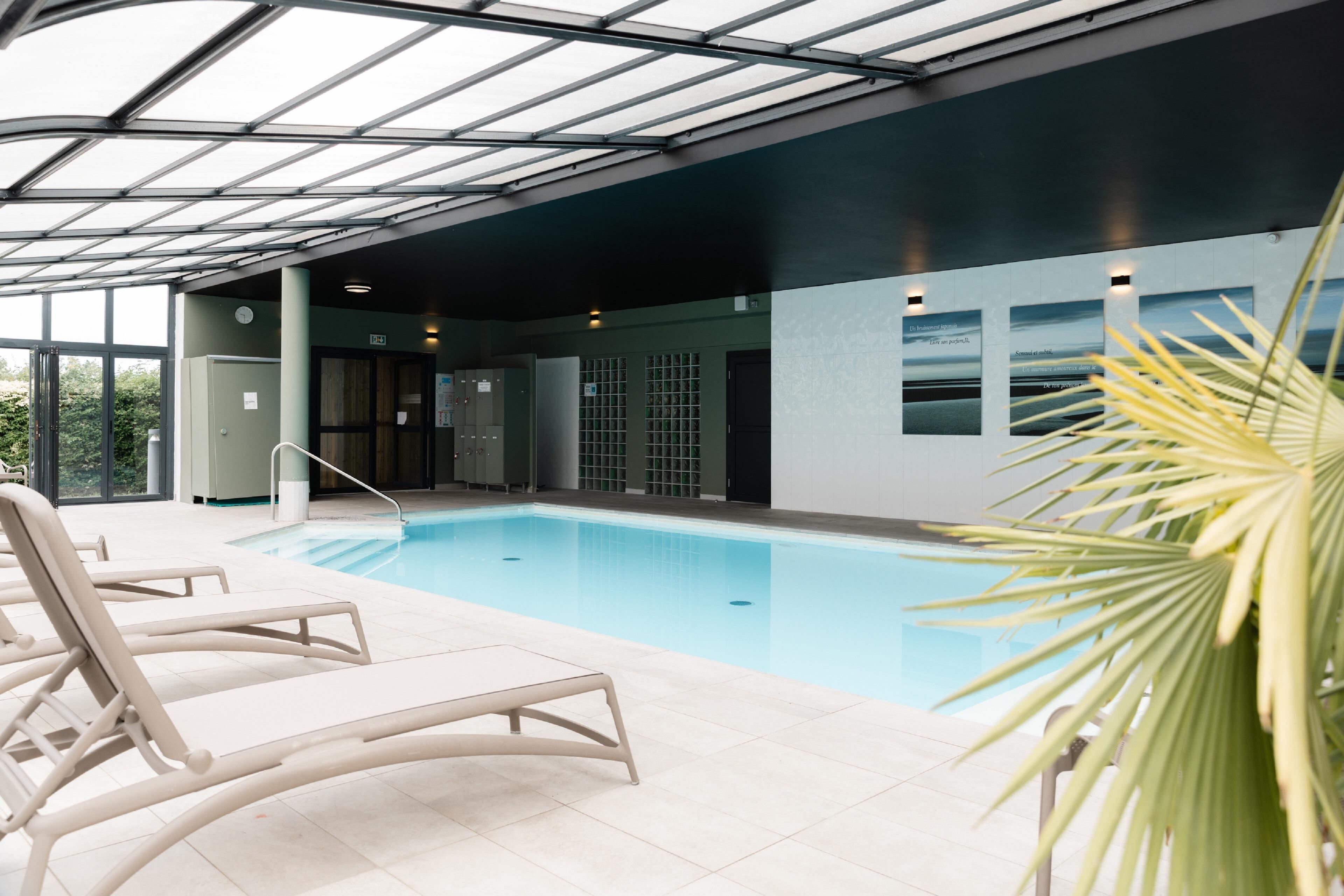 A swimming pool with lounge chairs, a glass ceiling, and a view of the outdoors.