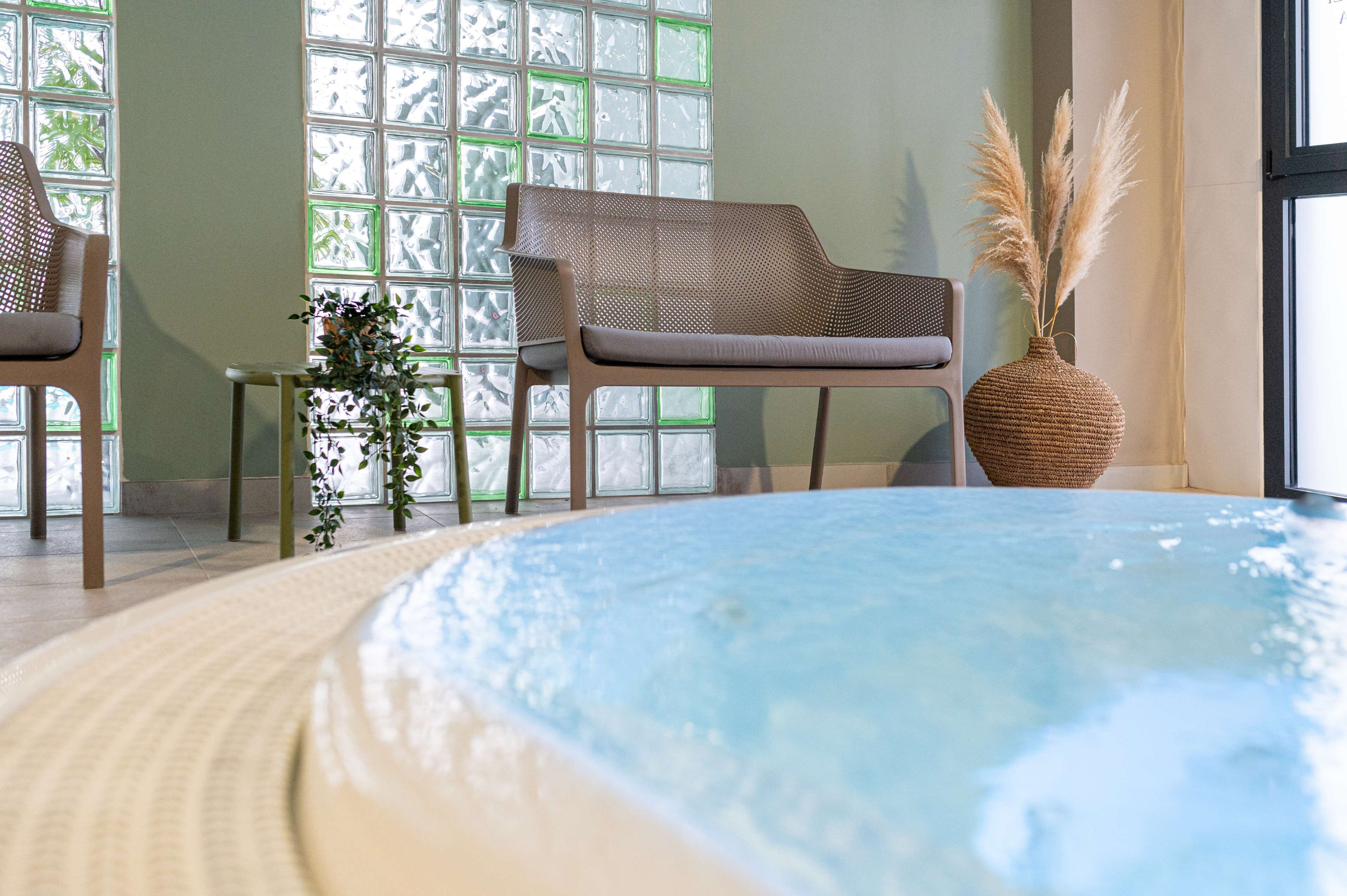 A spa area with a hot tub, wicker chairs, and a decorative vase with pampas grass.