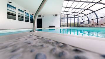 An indoor swimming pool with clear glass walls, a tiled floor, and a bench area.