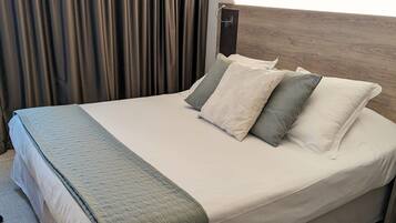 Un letto rifatto con una coperta trapuntata e cuscini, una testiera in legno e un quadro appeso sopra il letto.