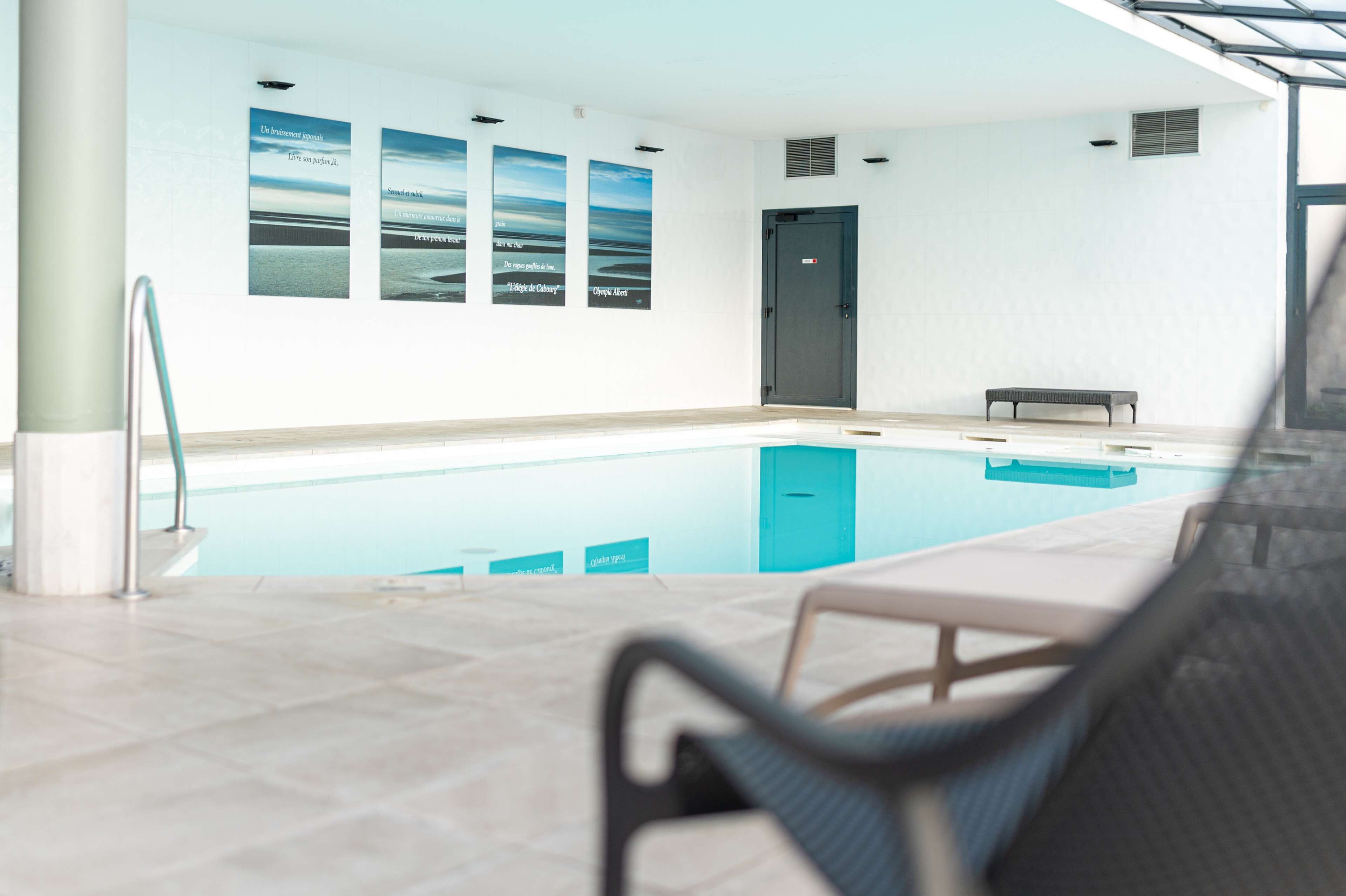Une piscine intérieure avec un banc et une chaise, une porte, et trois tableaux encadrés accrochés au mur.