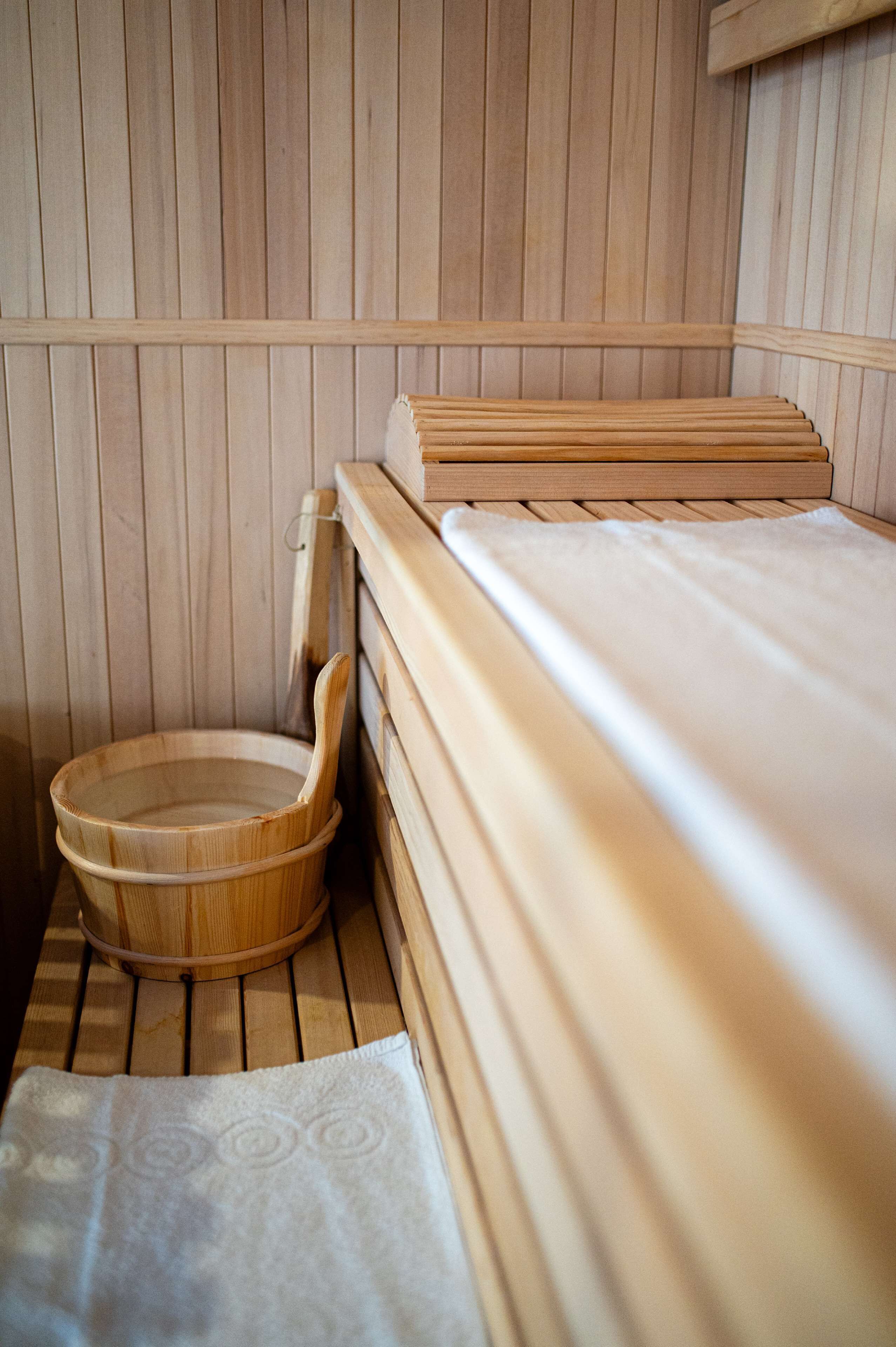 A wooden sauna room with a bench, a wooden basin, and a towel.
