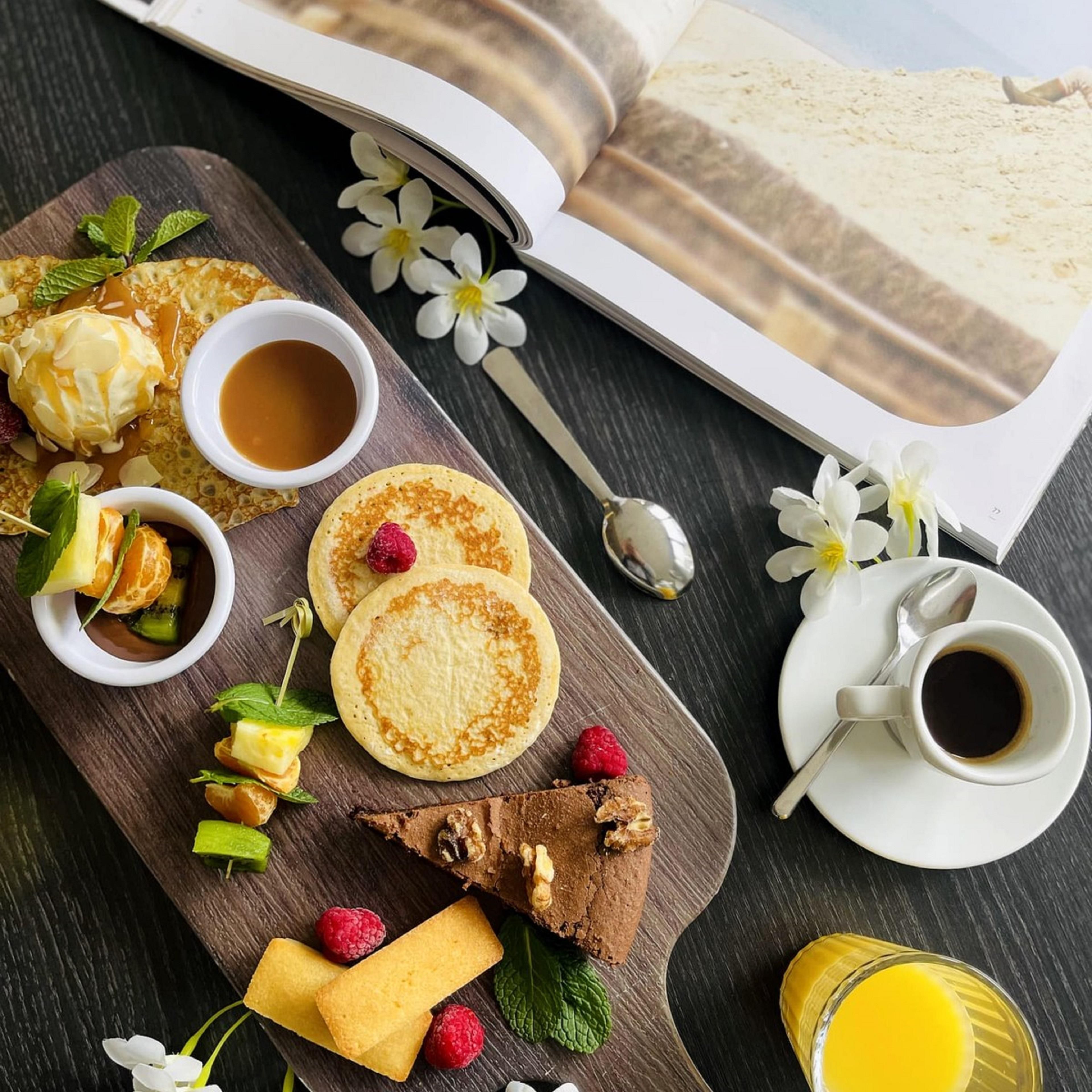 Un desayuno servido sobre una tabla de madera con panqueques, fruta y bebidas.